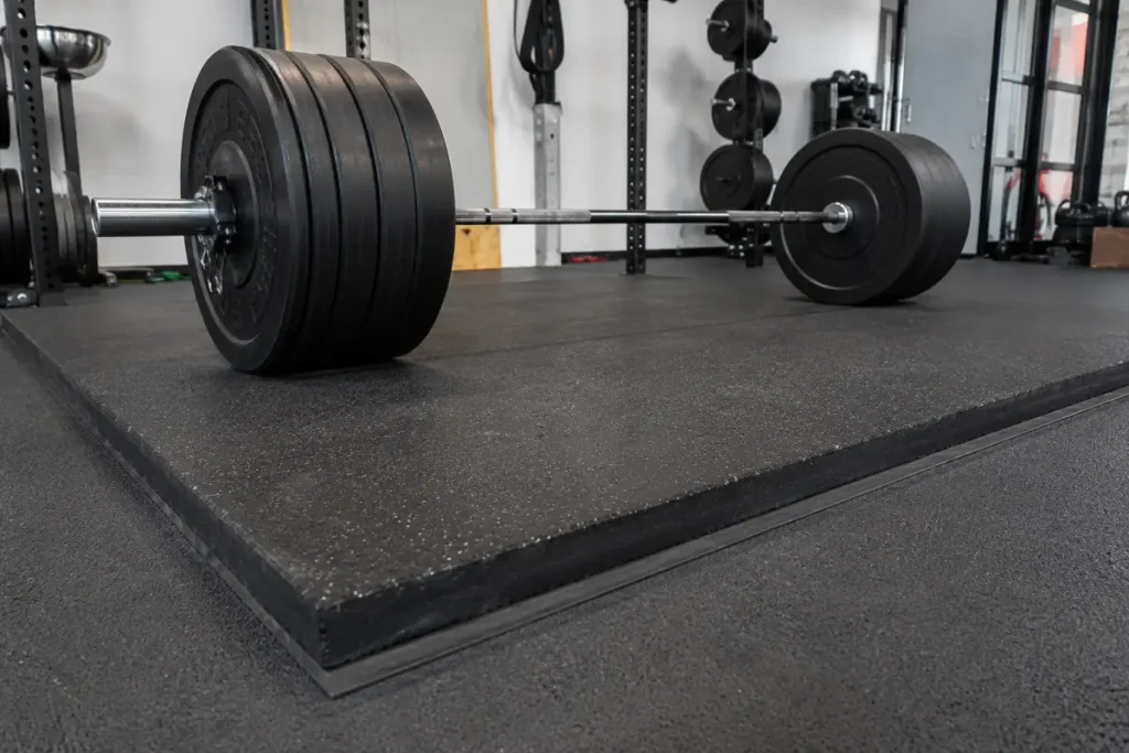 A heavy-lifting platform of thick rubber matting under a loaded barbell
