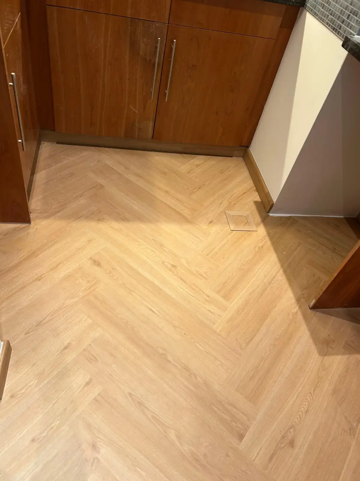 Herringbone SPC flooring neatly cut around a floor access hatch in a Valia Tower kitchen, Dubai