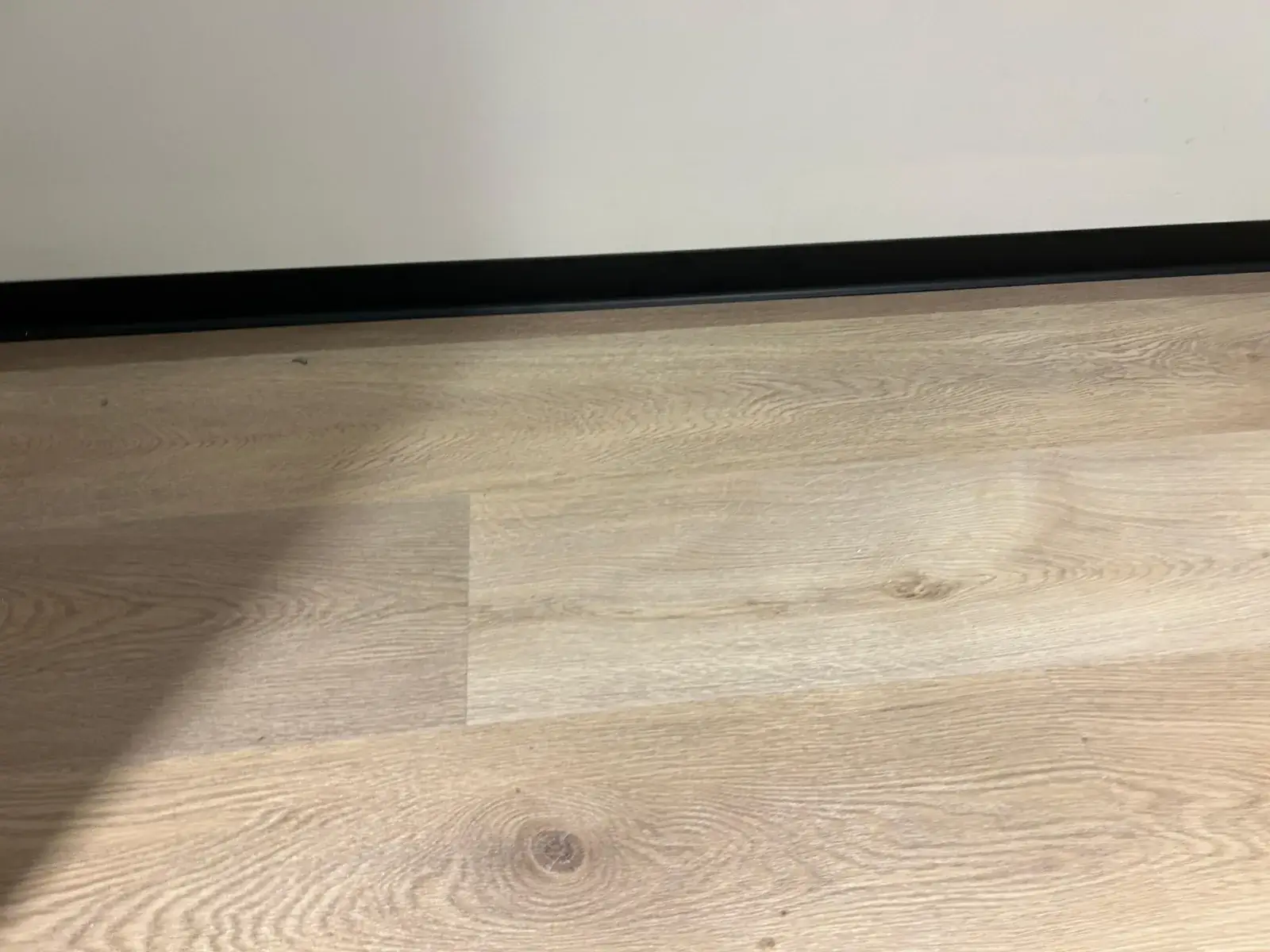 Close view of pale oak SPC plank grain against black skirting, Al Nahda 2 Dubai