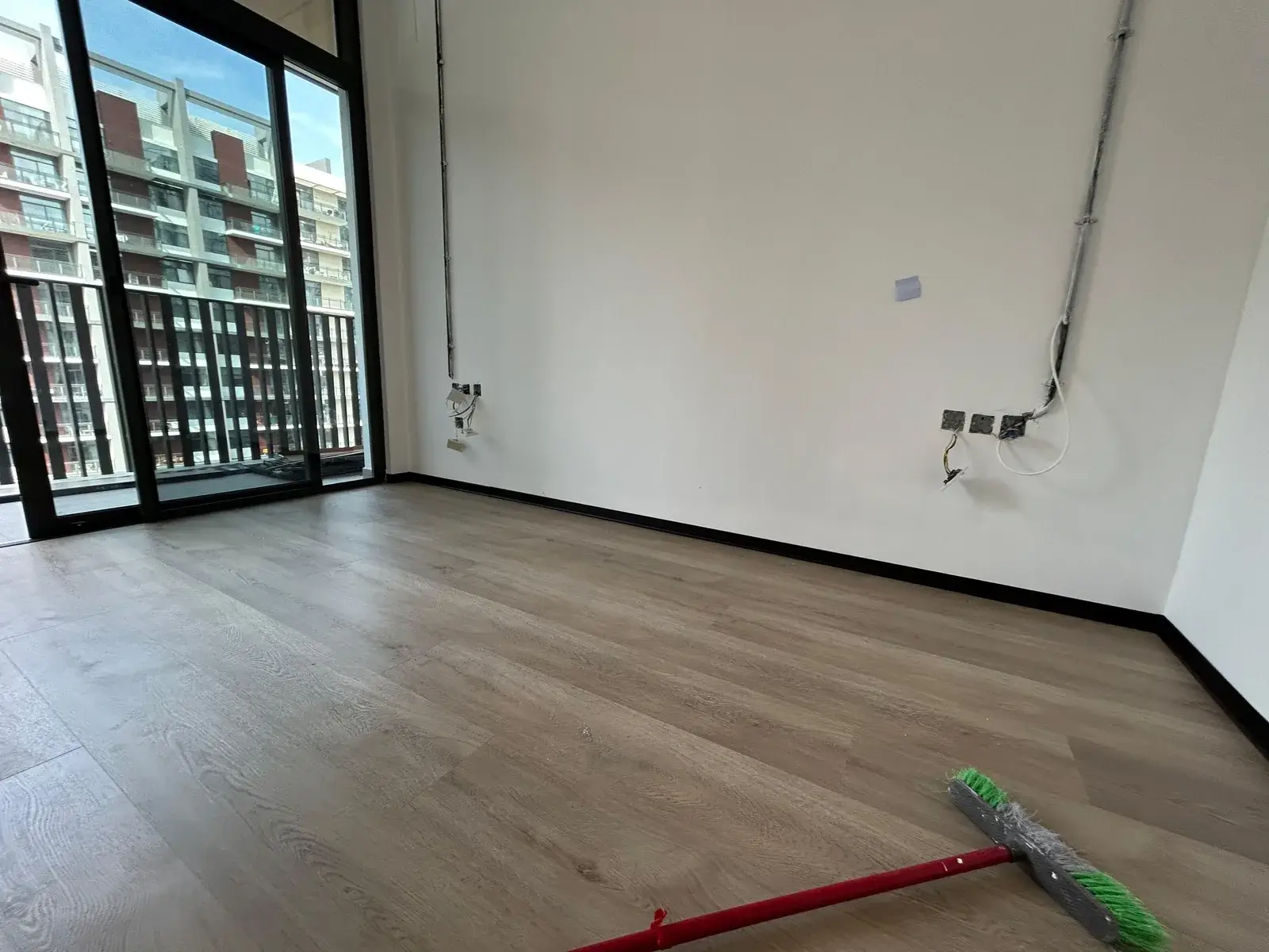 Pale oak SPC flooring in a new-build apartment living room with balcony doors, Al Nahda 2 Dubai