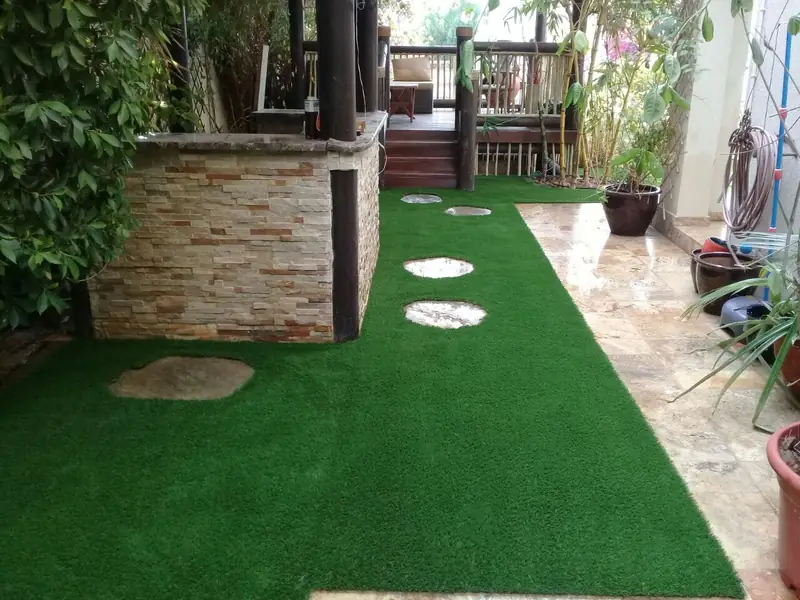 Artificial grass laid around round stepping stones in a Dubai villa courtyard beside a stone-clad planter