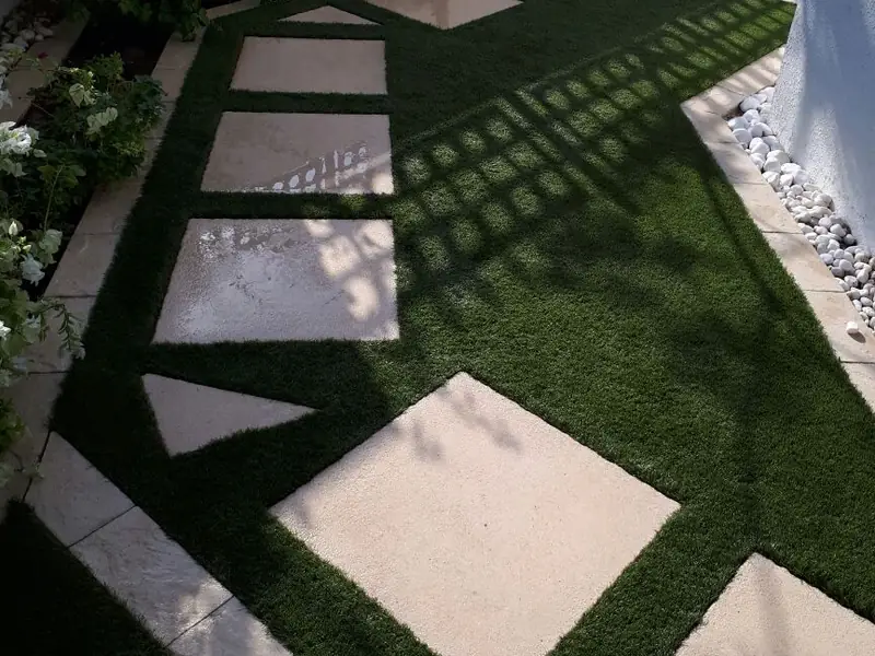 Artificial grass cut in around large rectangular stepping slabs on a villa garden path in Dubai