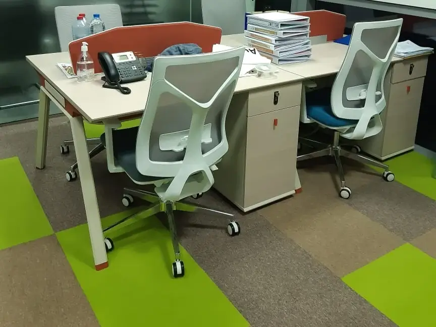 Office carpet tiles under a workstation cluster, with chair castors resting on the tiled floor