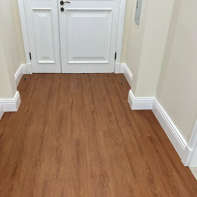 WPC plank flooring in an apartment corridor meeting retained stone at the door openings, JVT Dubai